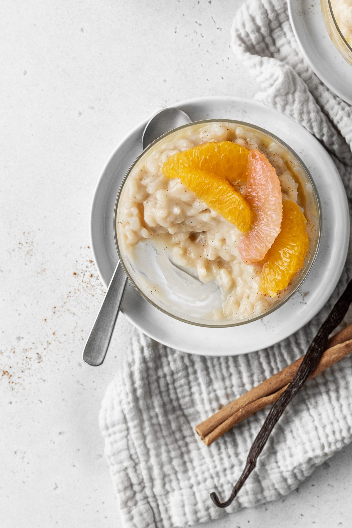 A half eaten glass of vegan rice pudding with citrus segments on top.