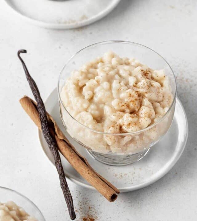 A bowl of vegan rice pudding with a cinnamon stick and vanilla bean