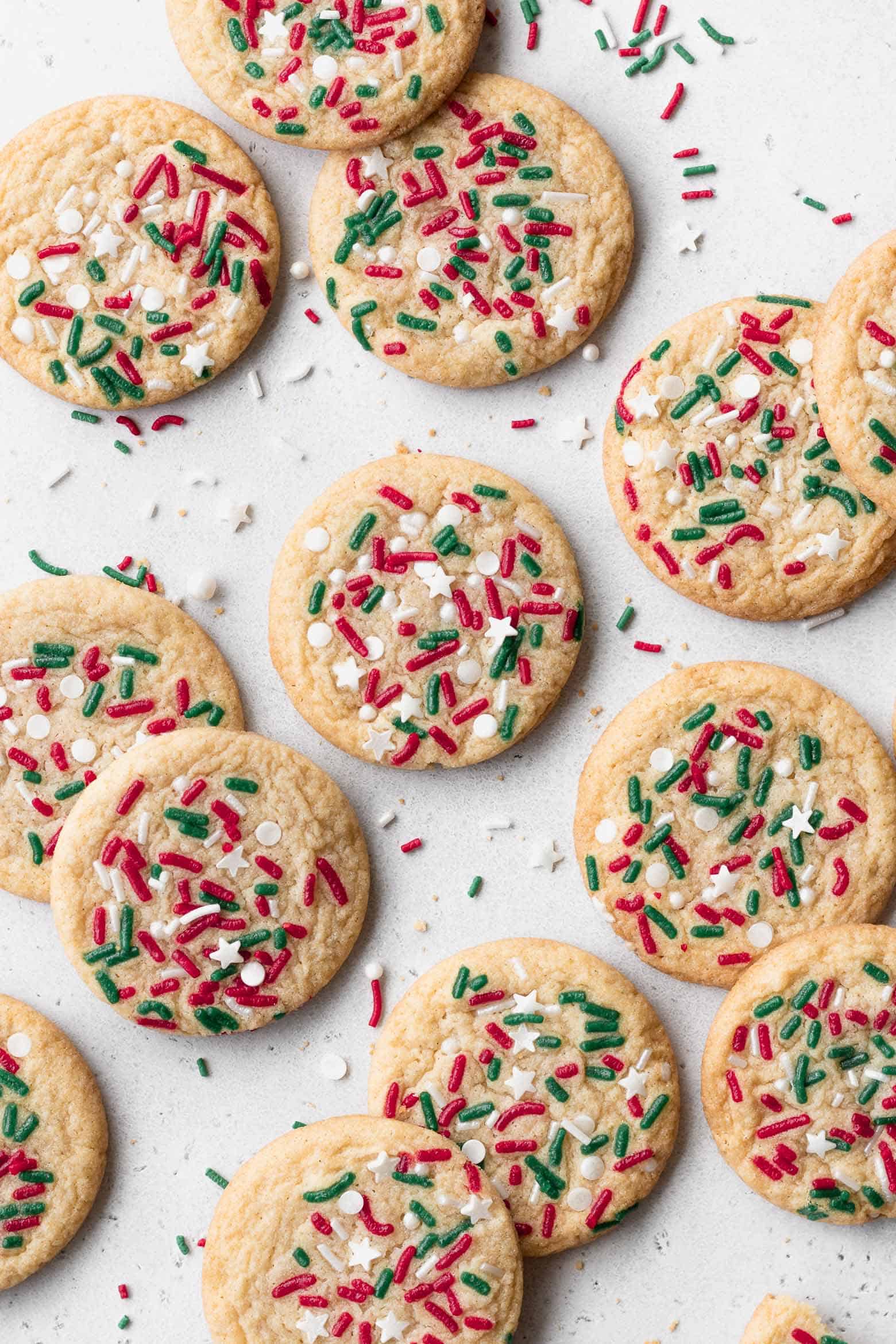 Christmas sugar cookies with sprinkles on a white surface.