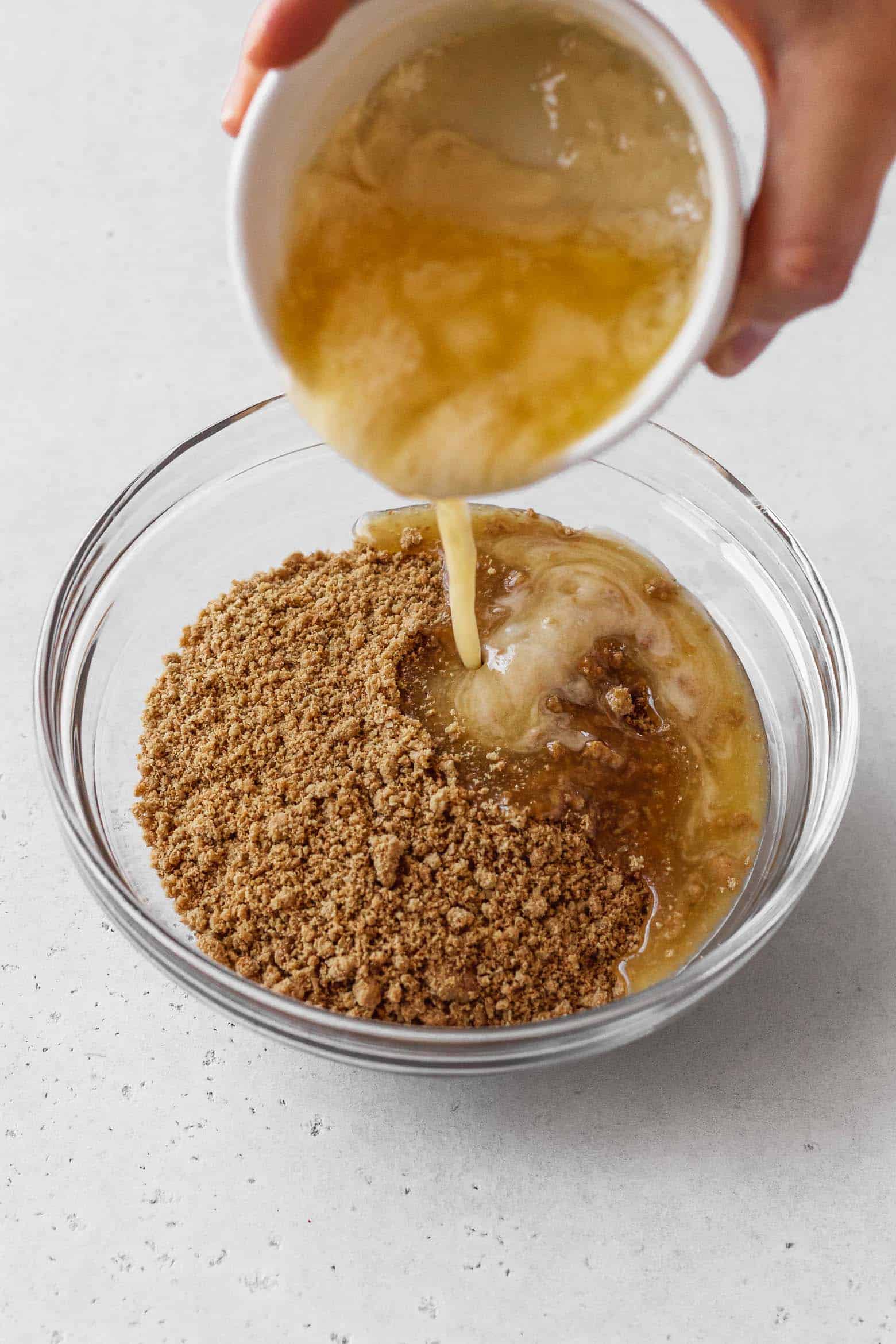Melted butter being poured into a bowl of graham cracker crumbs.