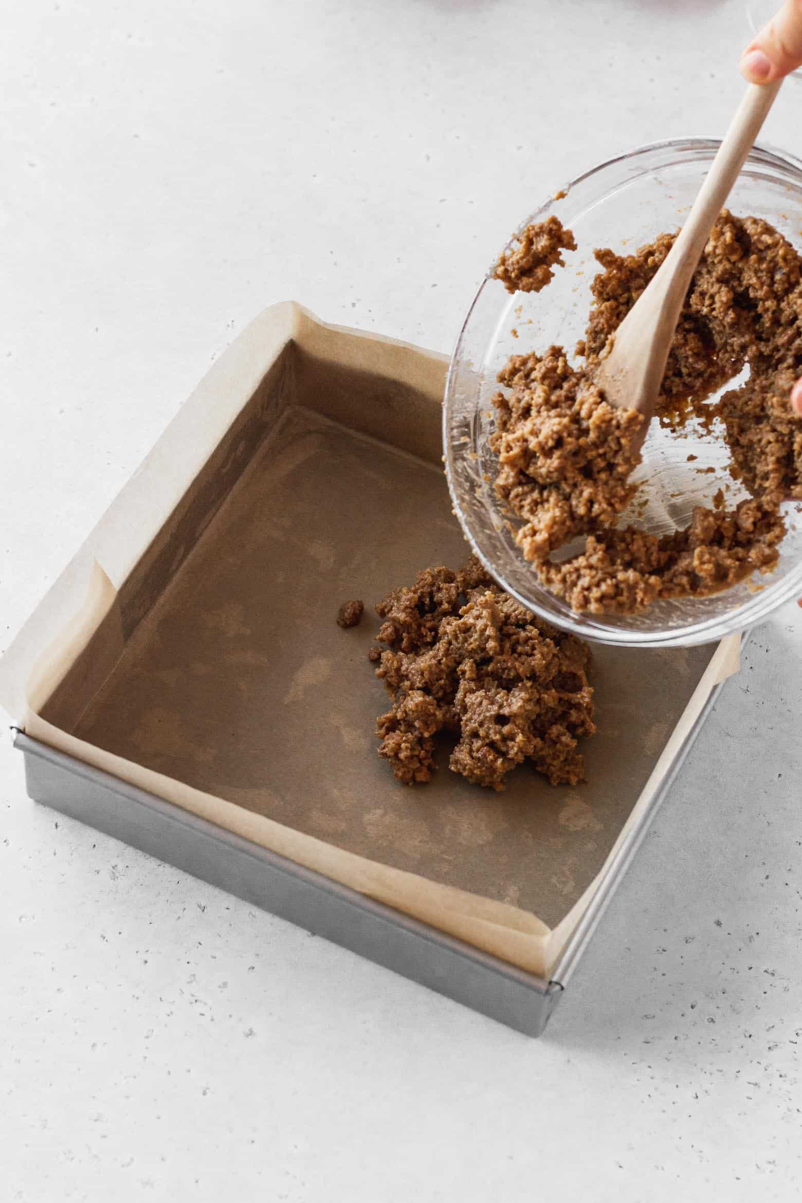 Putting the graham cracker mixture into a square pan.