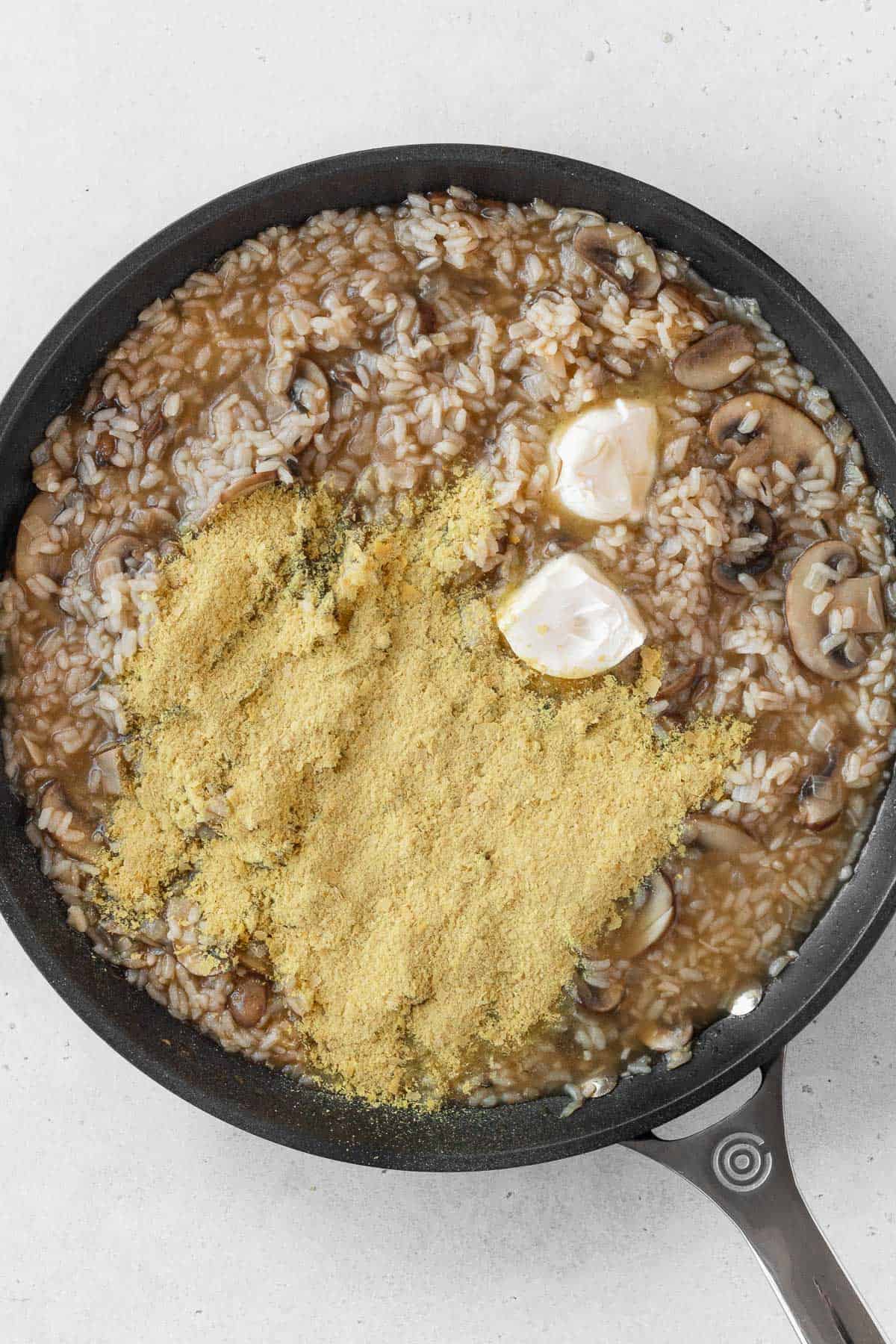 Butter and nutritional yeast on top of mushroom risotto in a pan.