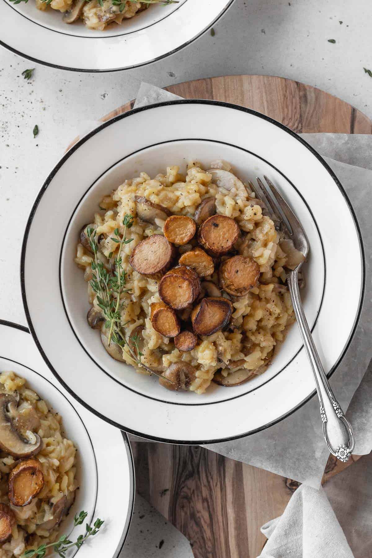 A white bowl of vegan mushroom risotto with a silver fork.