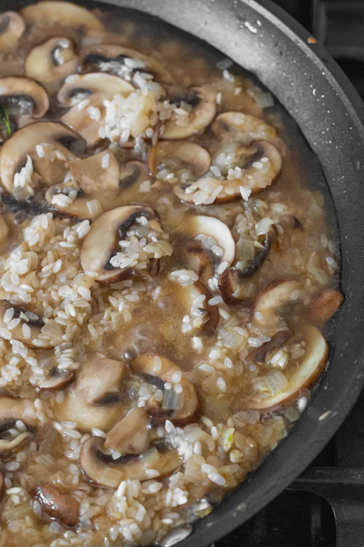 Vegetable stock added to the pan with mushroom and rice.