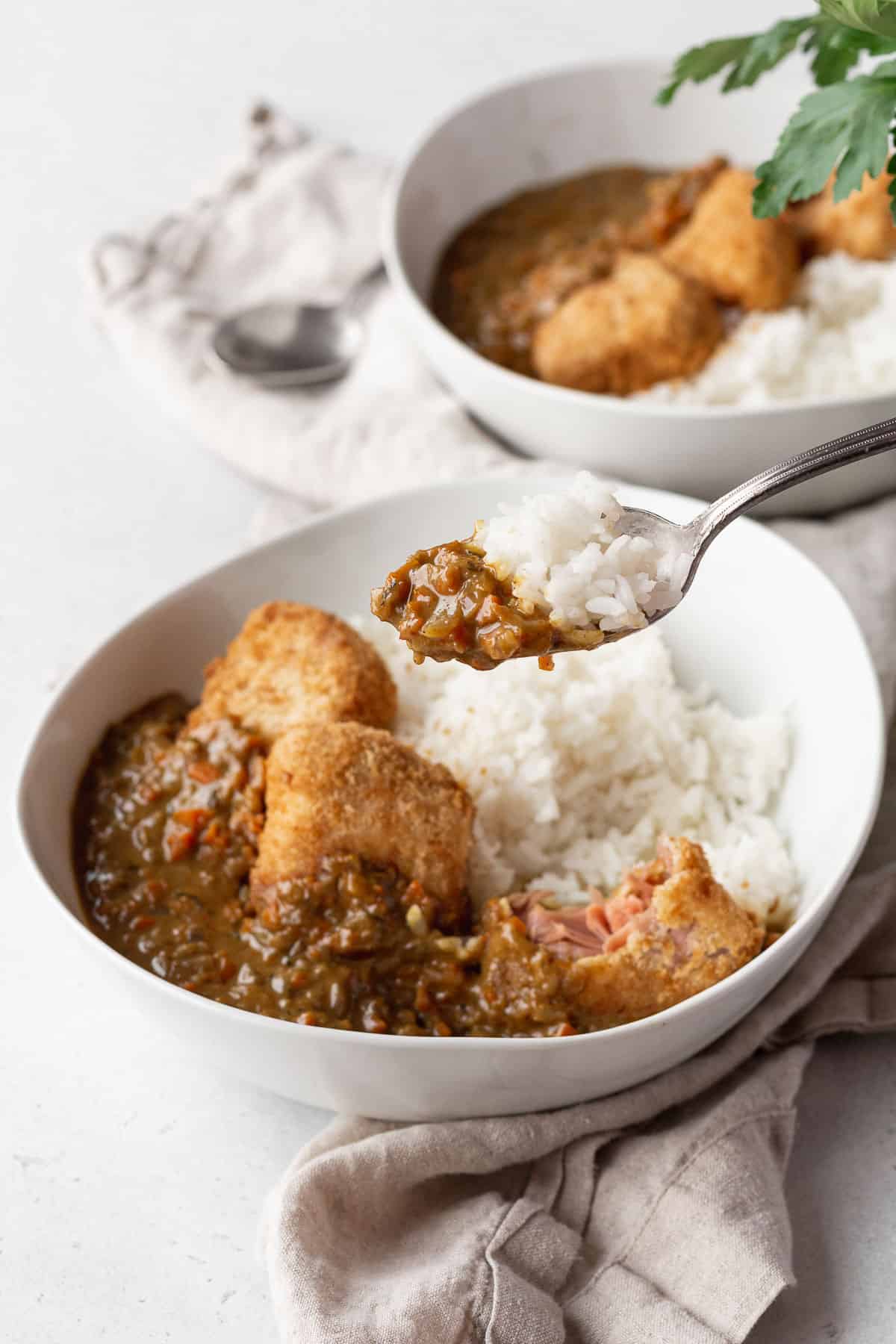 A bowl of vegan katsu curry with a spoon holding some rice and curry.