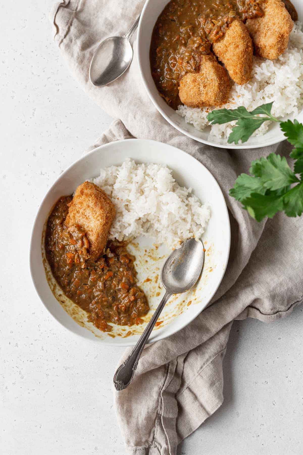 2 bowls of katsu curry on a natural linen with a silver spoon.