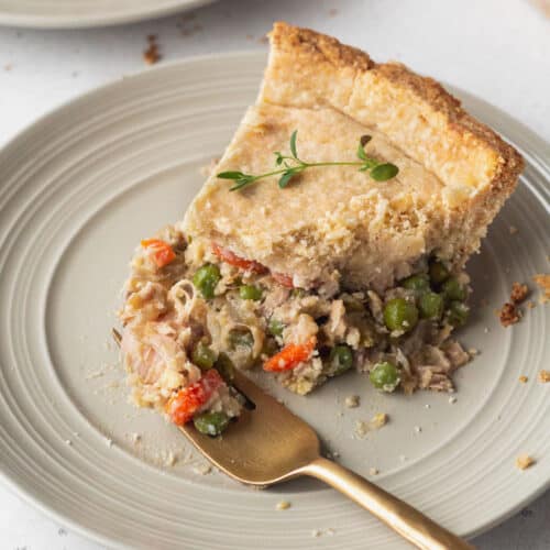 A slice of vegan chicken pot pie on a plate with a bite on a gold fork.