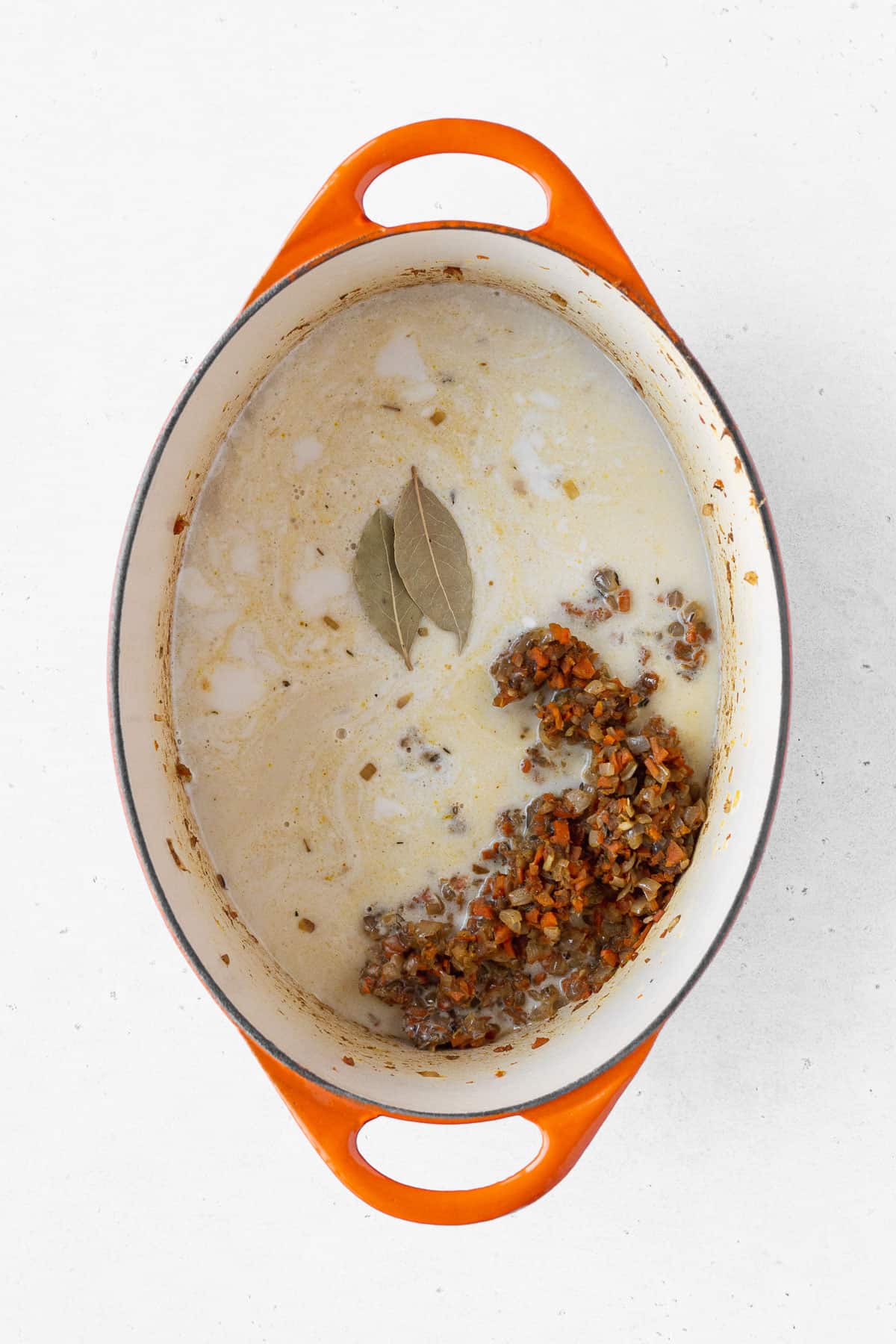 Coconut milk and vegetable stock poured over the vegetables, with two bay leaves added on top.