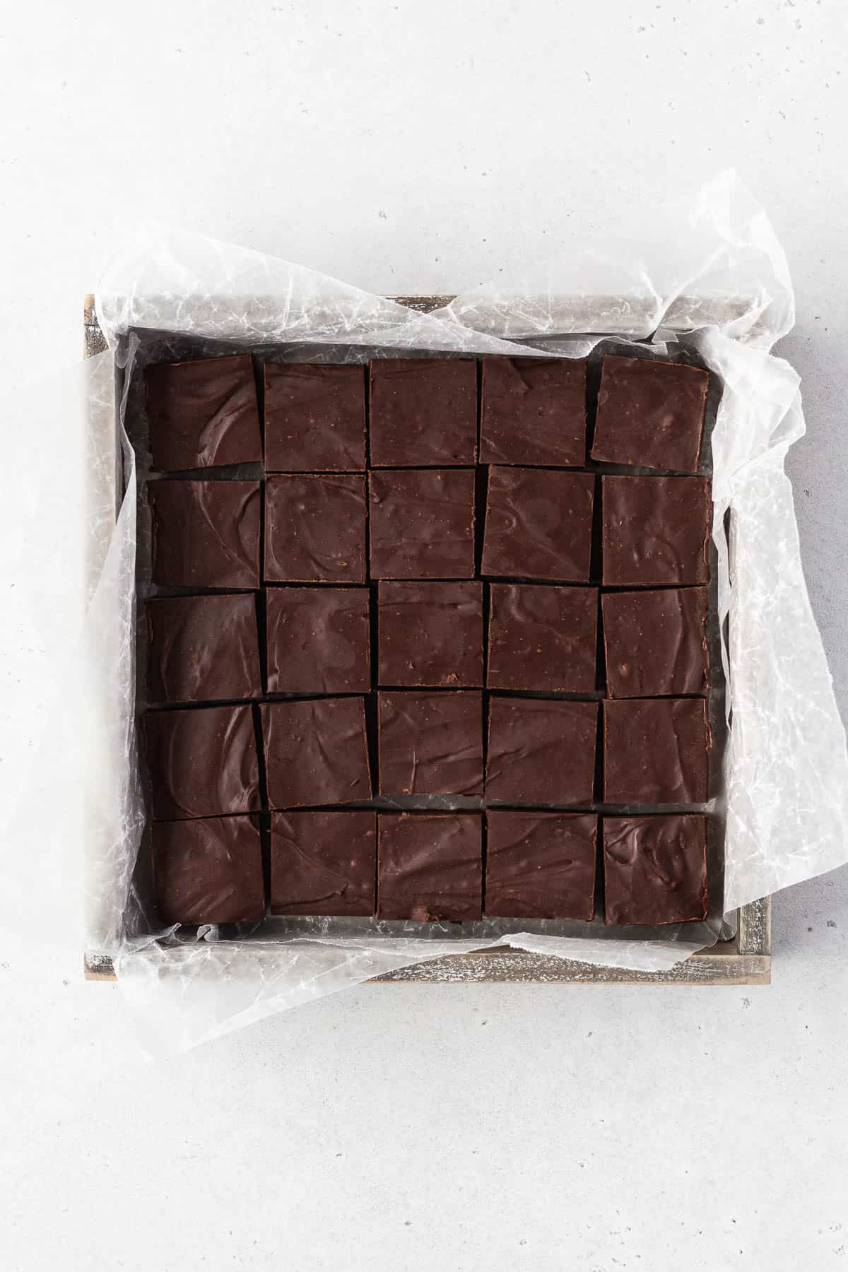 Finished batch of dairy-free vegan fudge in a wooden box with parchment paper after being cut into squares.