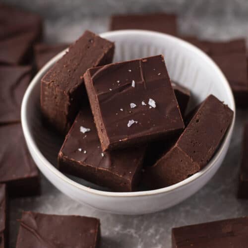 Closeup shot of cubes of dairy-free fudge in a white bowl and garnished with some flaky sea salt.