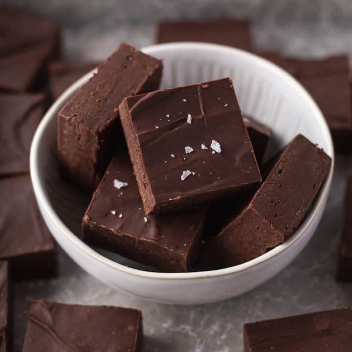 Closeup shot of cubes of dairy-free fudge in a white bowl and garnished with some flaky sea salt.