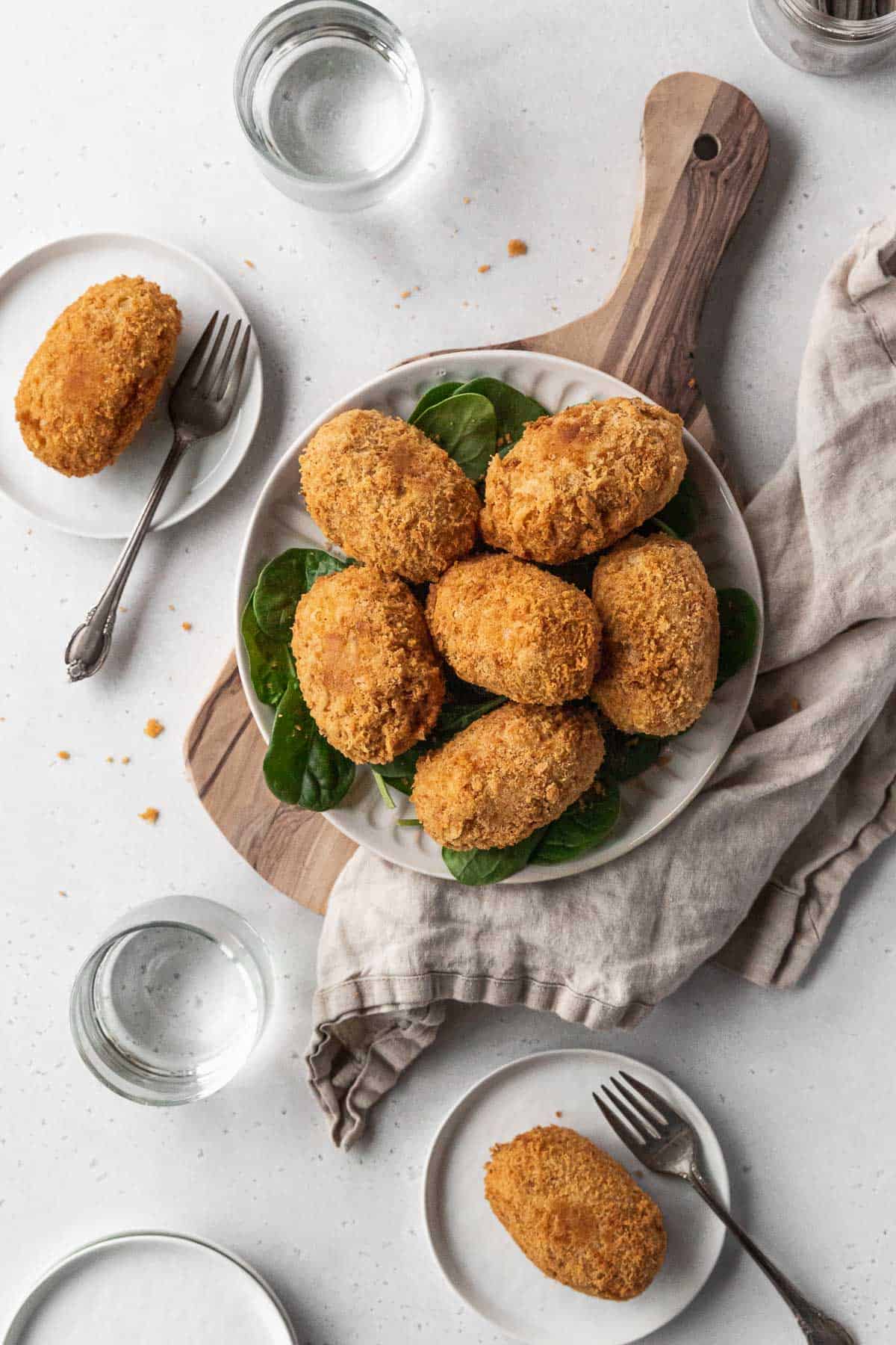 Overhead hero shot of a serving platter of vegan potato croquettes on a table with two plated up on smaller appetizer plates.