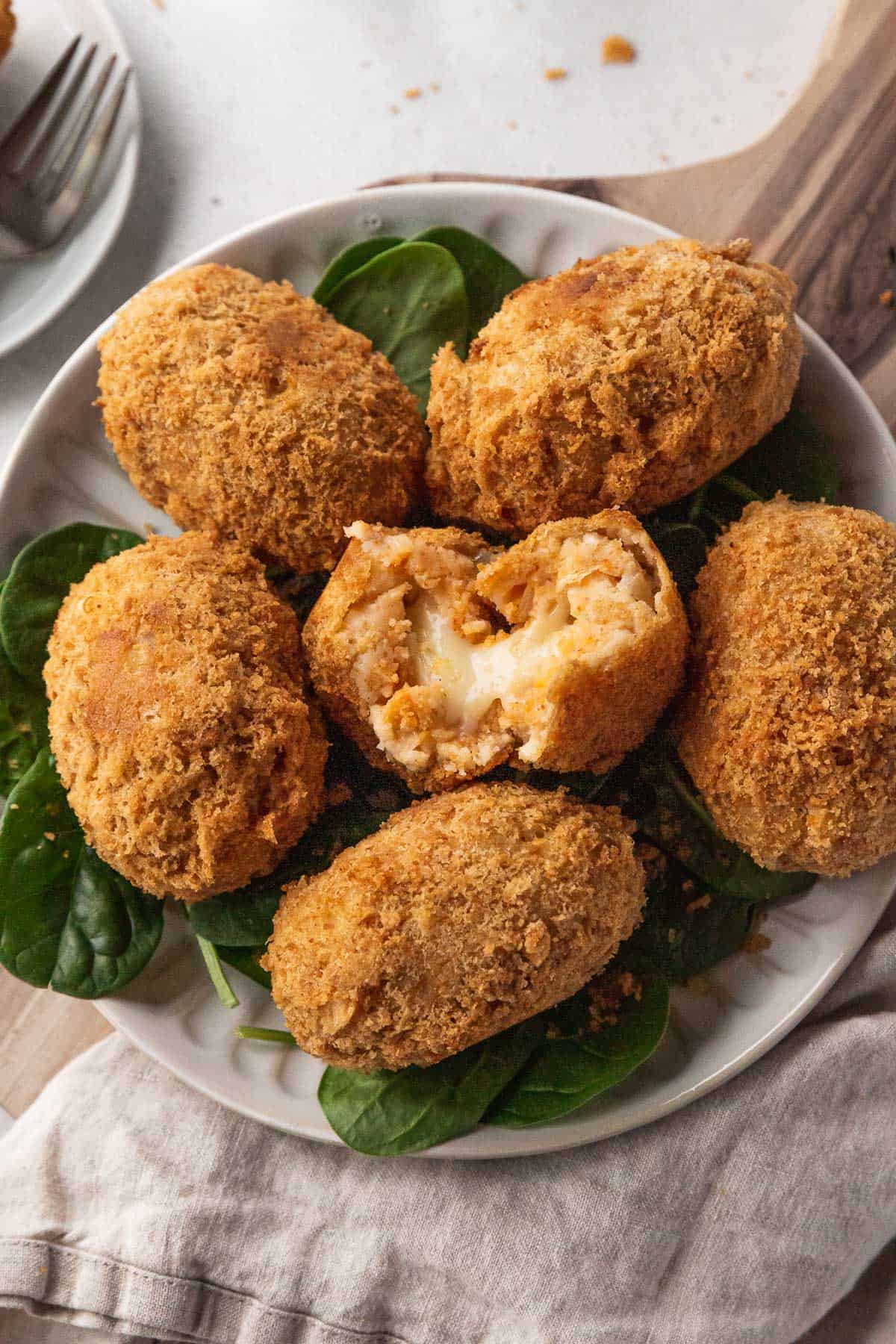 Closeup on serving platter of potato croquettes with the center one broken open to reveal the gooey, cheesy center.