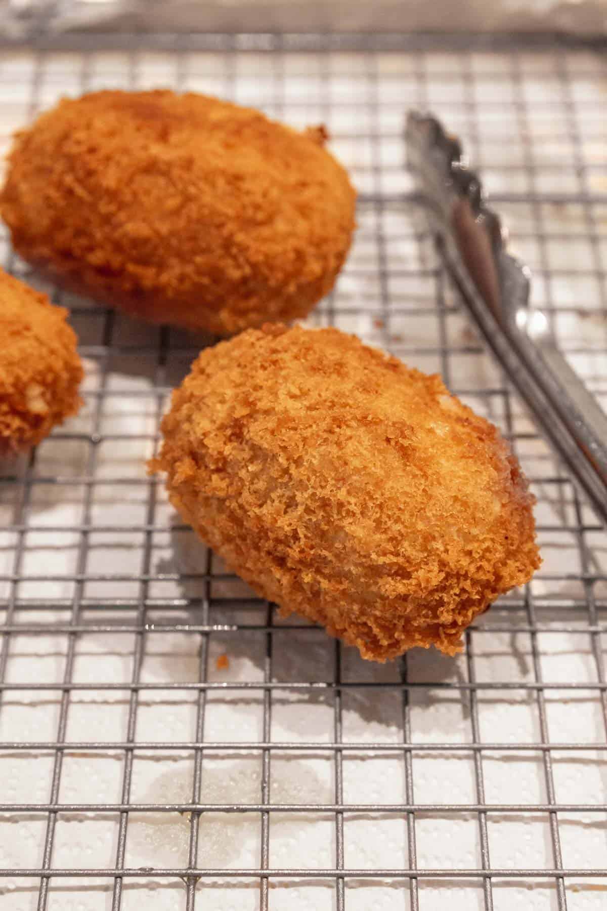 Close up shot of a golden, crispy potato croquette draining on a wire rack above paper towels.