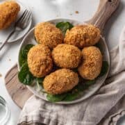 Vegan curry potato croquettes on a serving platter atop a wooden cutting board.
