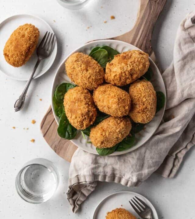 Overhead hero shot of a serving platter of vegan potato croquettes on a table with two plated up on smaller appetizer plates.