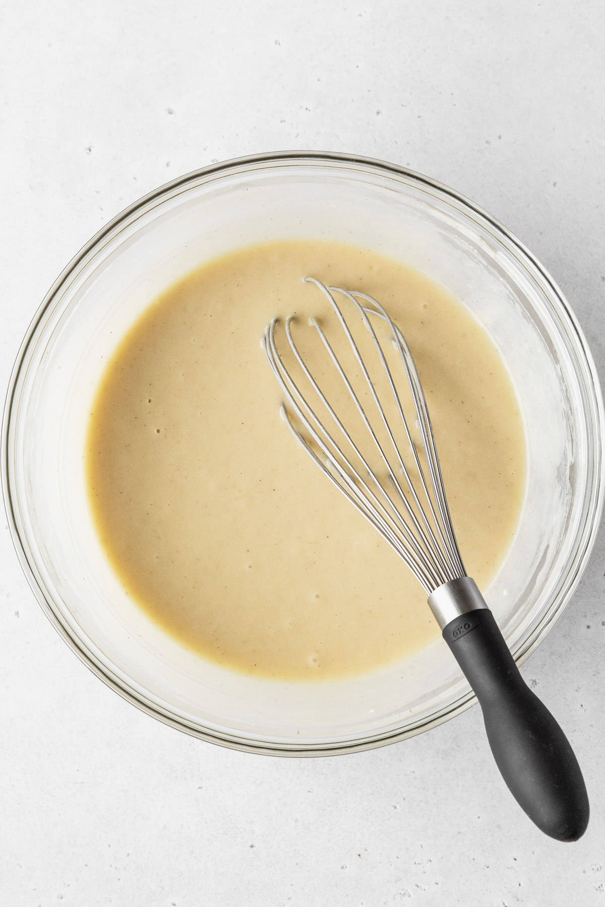 Completed dairy free vanilla cupcake batter in a clear mixing bowl with a black-handled whisk.
