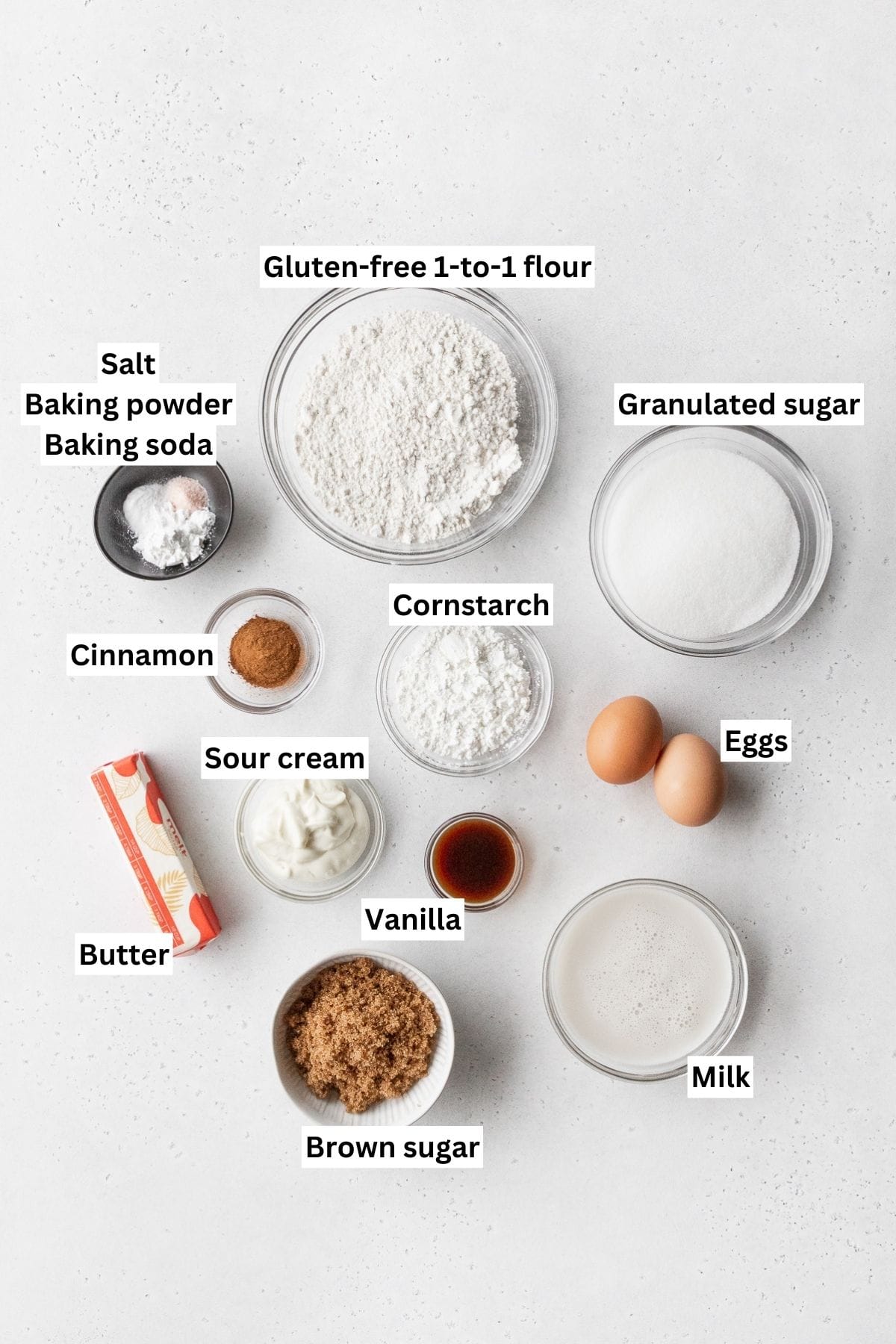Ingredients for making gluten-free coffee cake with crumb topping measured out into small bowls and laid on a white tabletop.