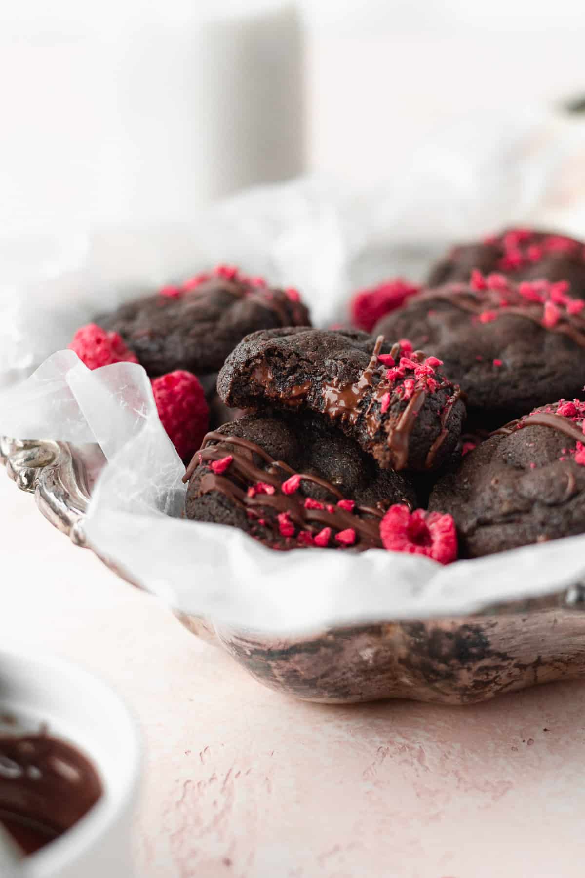 A silver dish with gluten free chocolate cookies, with a bitten cookie on top with melted chocolate chips.