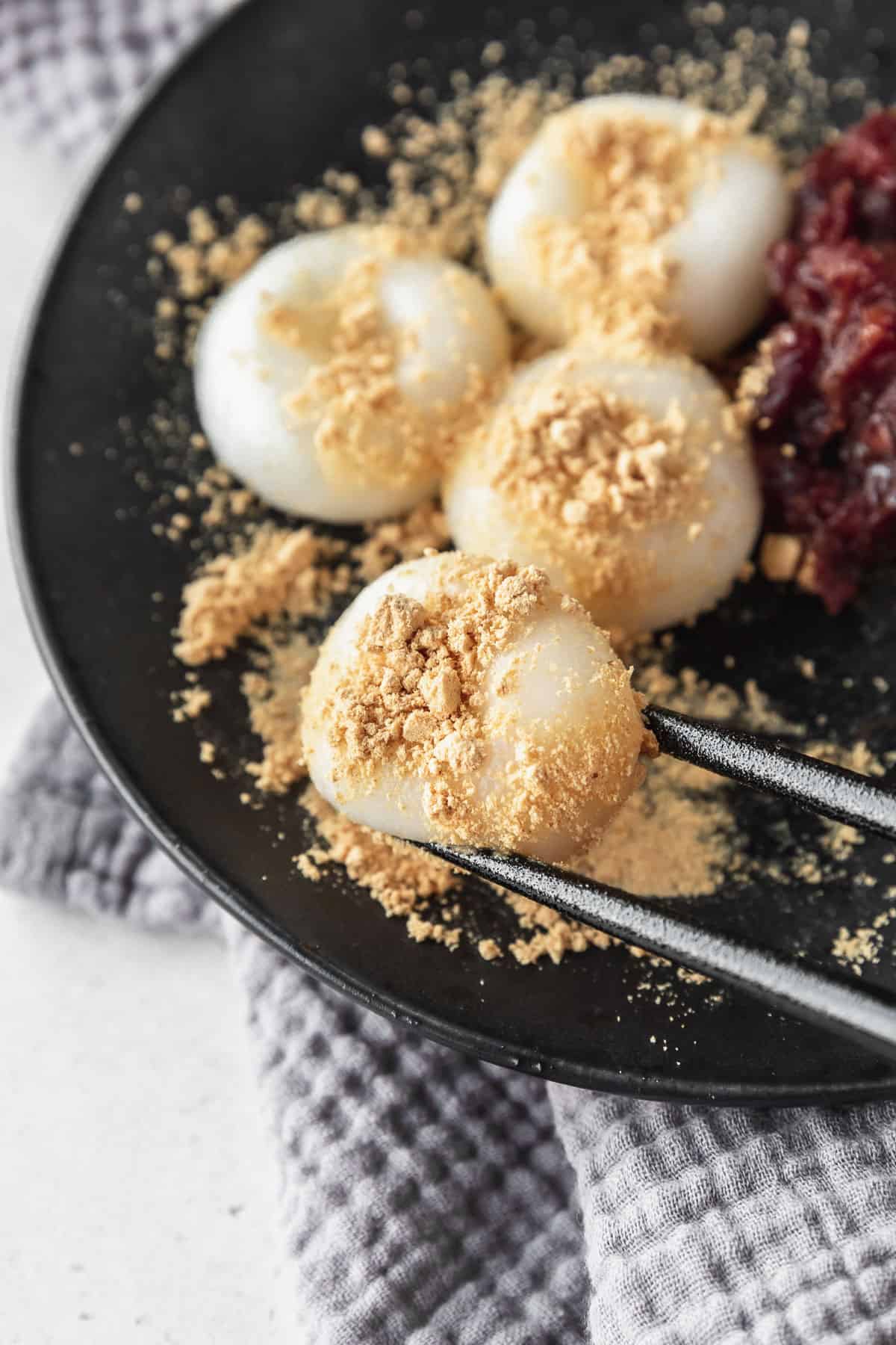Black chopsticks picking up a shiratama dango with kinako powder on top.