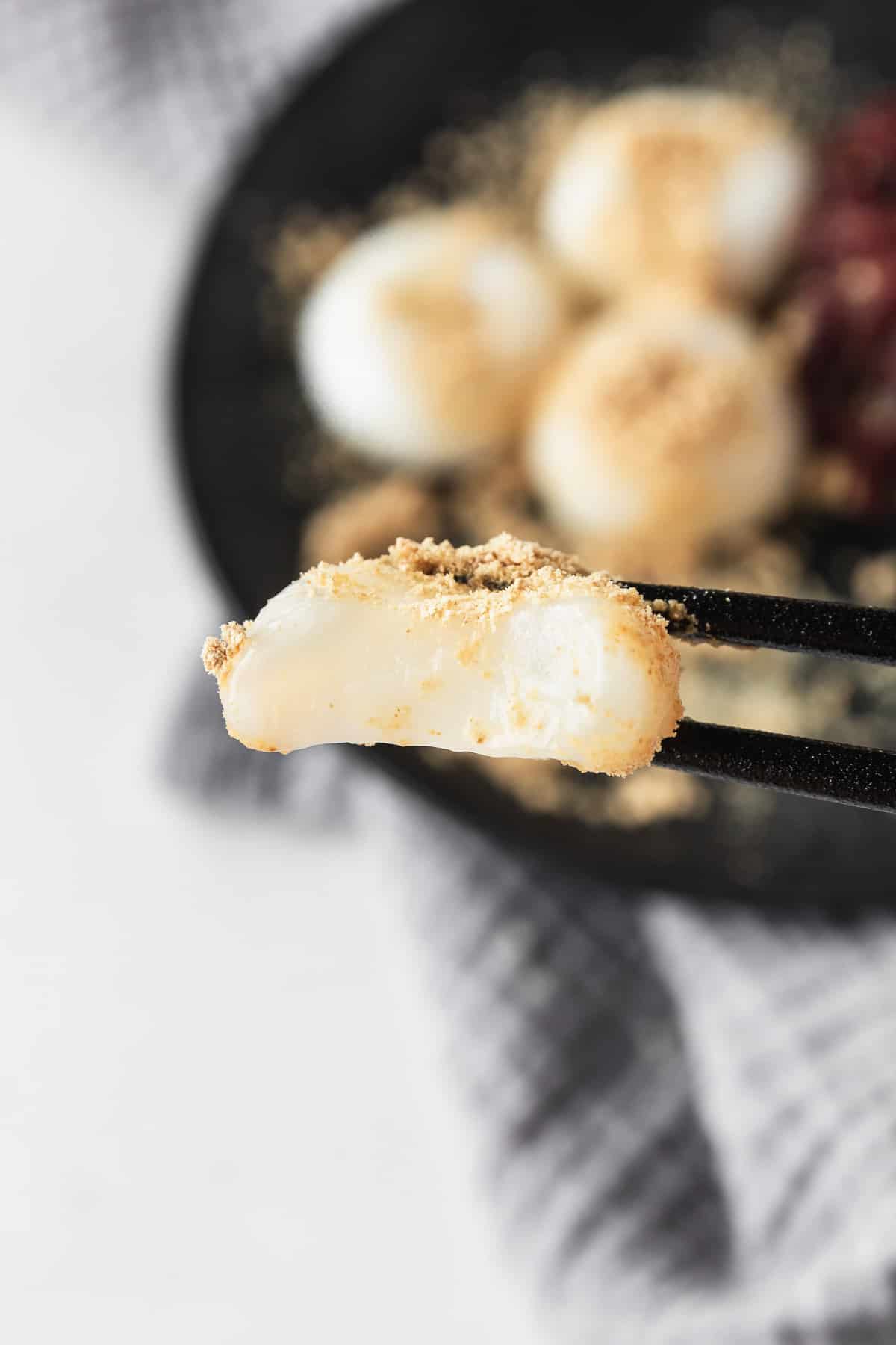 A bitten shiratama mochi being held by black chopsticks.