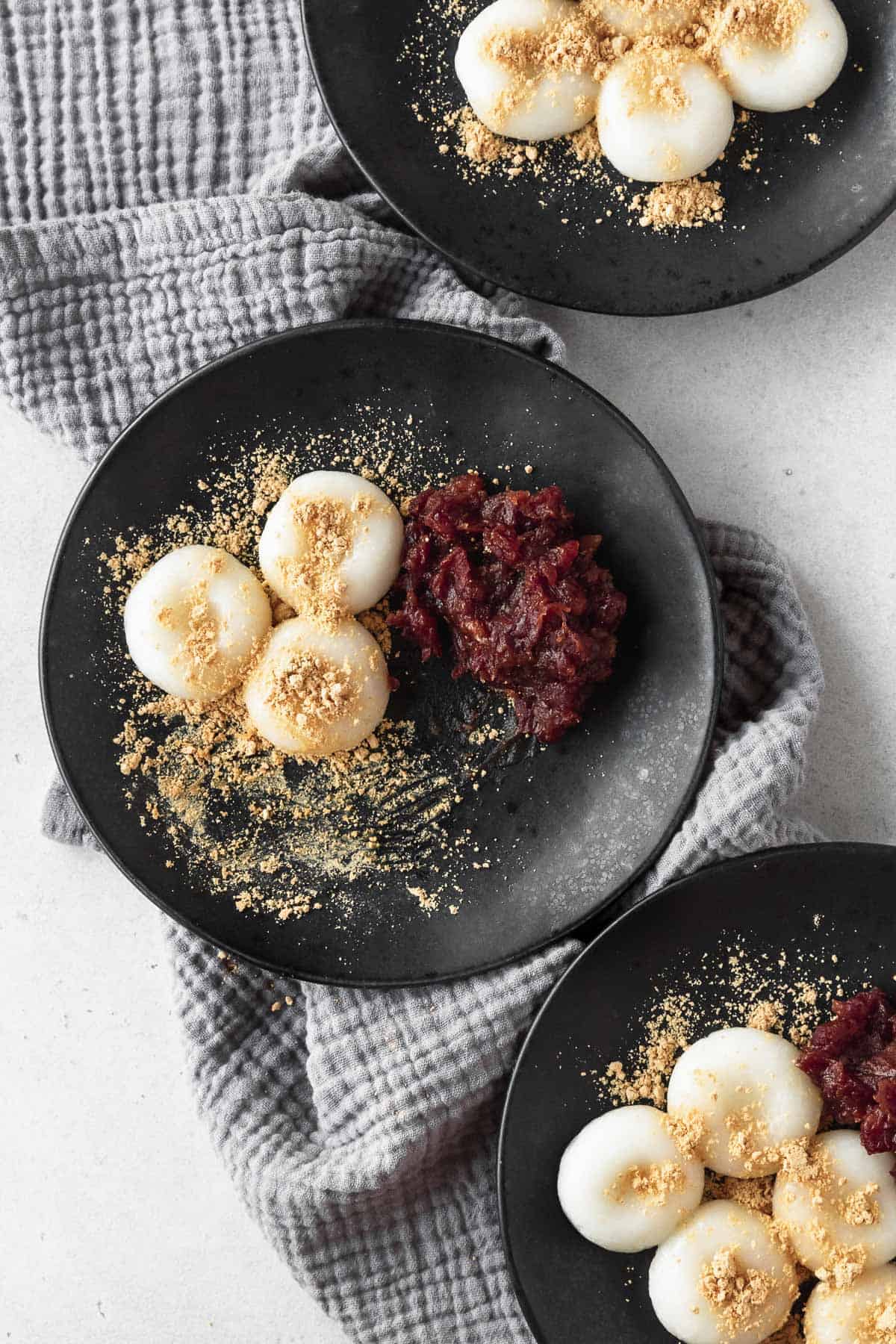 A half eaten black plate of shiratama and anko on a grey linen napkin.