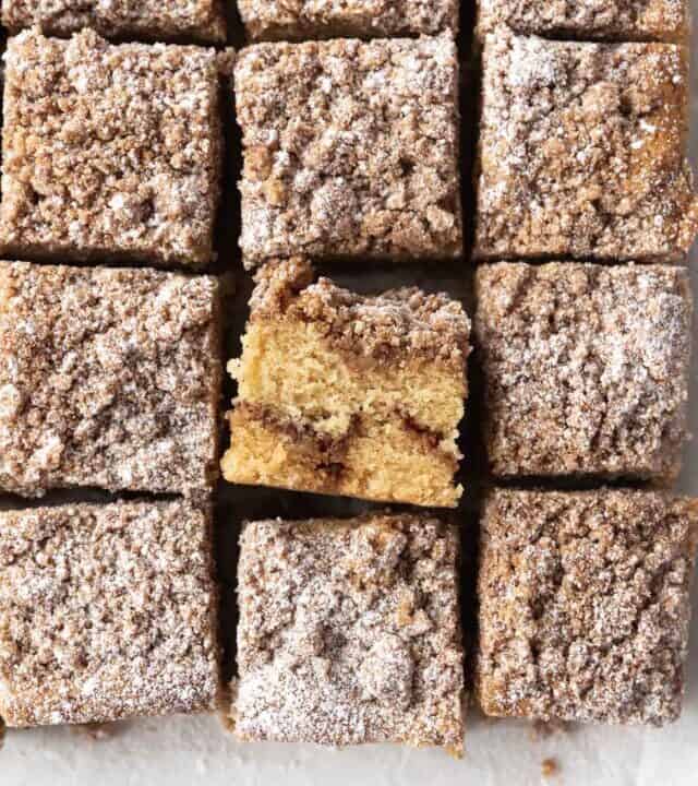overhead shot of gluten-free coffee cake cut into 12 squares with one flipped sideways to show the ribbon of cinnamon sugar filling running through it.