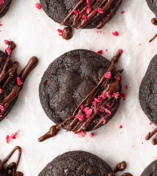 A close up shot of gluten-free double chocolate chip cookies with freeze-dried raspberries sprinkled on top.