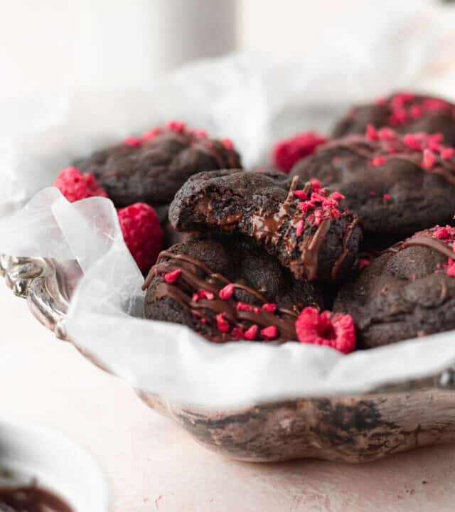 A silver dish with gluten free chocolate cookies, with a bitten cookie on top with melted chocolate chips.