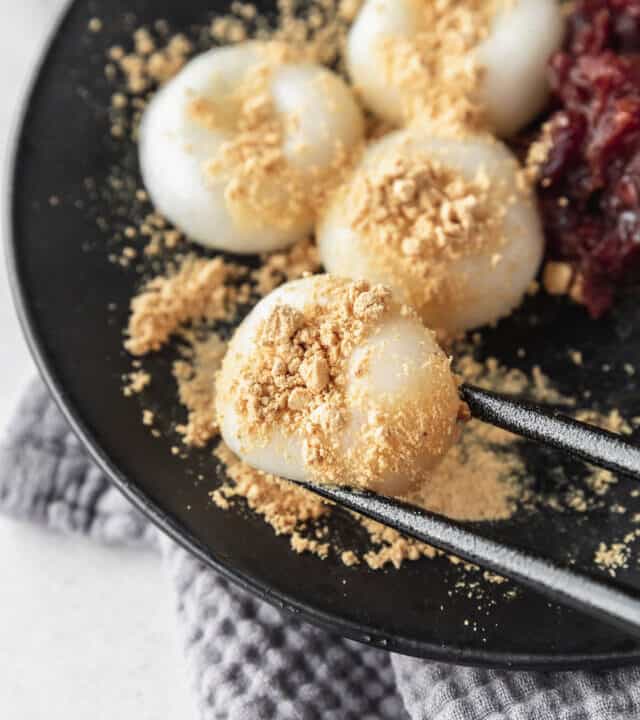 Black chopsticks picking up a shiratama dango with kinako powder on top.