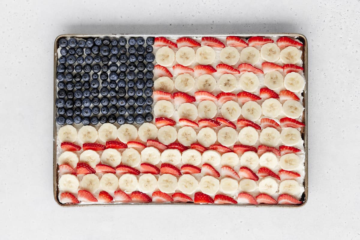 alternating rows of bananas and strawberries added to fill out the rest of the sheet pan frame and finish the fruit cookie pizza design.