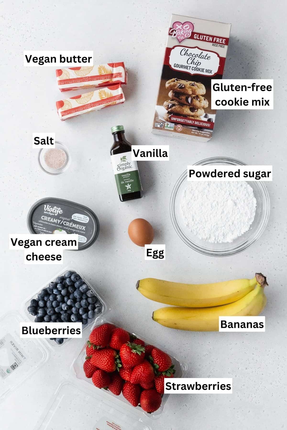 ingredients for making sugar cookie fruit flag dessert pizza laid out on a white table with text overlay.