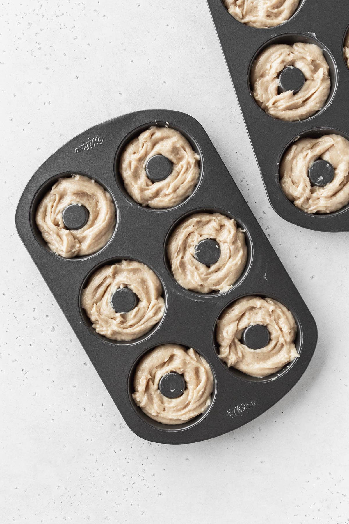 Overhead shot of unbaked dairy-free donut batter in two donut pans.