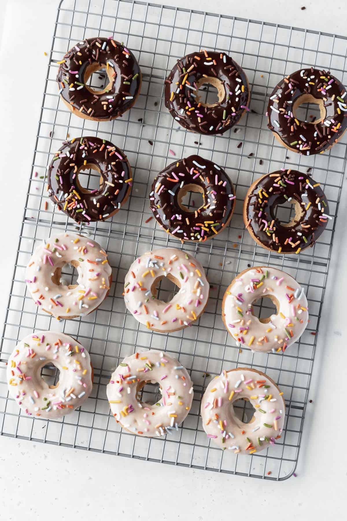 Overhead shot of 6 chocolate glazed and 6 vanilla glazed dairy free vegan donuts on a cooling rack.