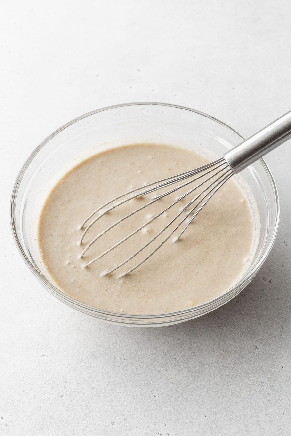 Vegan bread pudding batter being mixed with a whisk in a glass bowl.