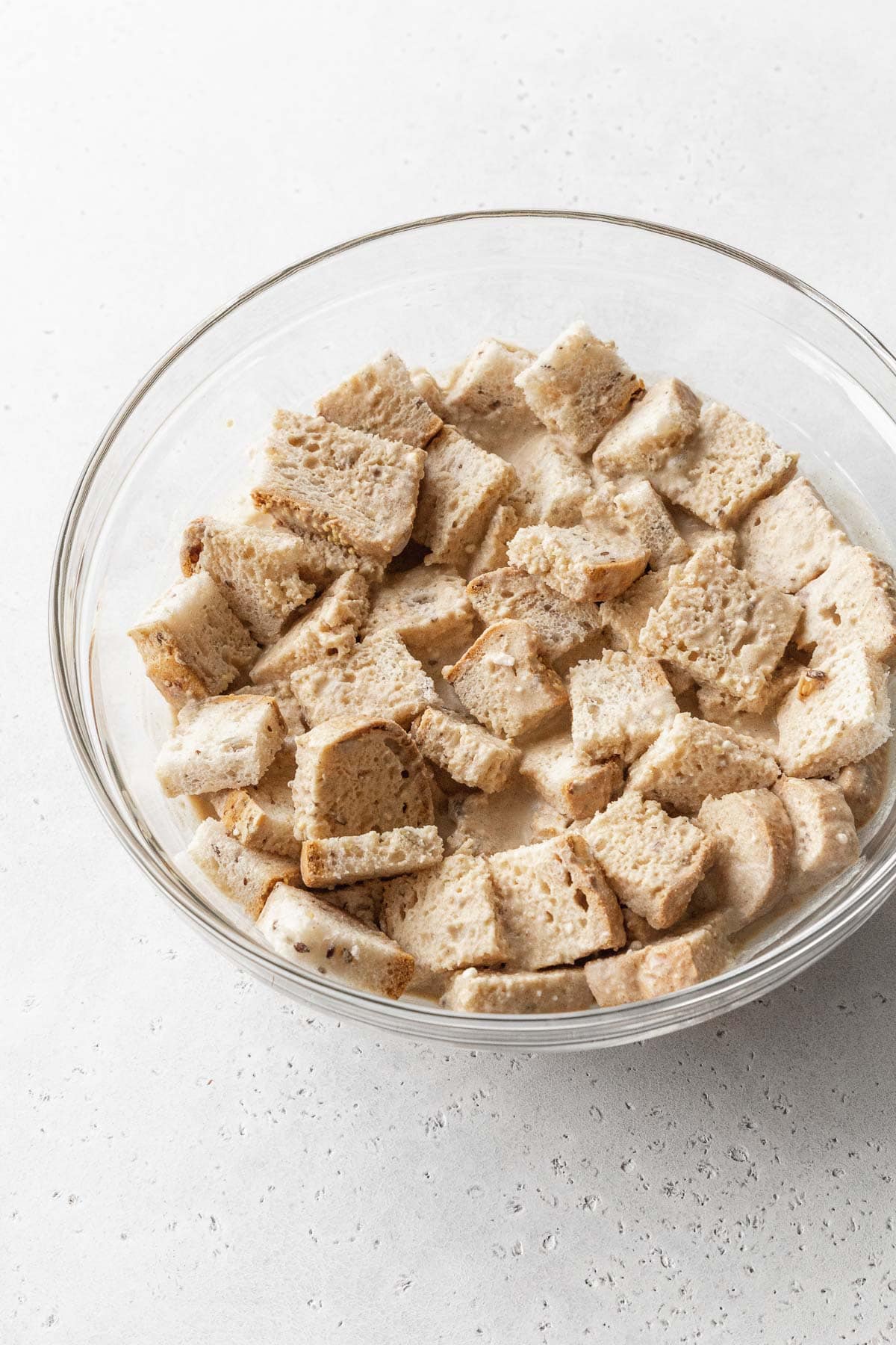 Cubed bread soaking in vegan bread pudding batter.