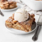 Slice of apple pie vegan bread pudding on a white dessert plate, topped with a scoop of vegan ice cream.