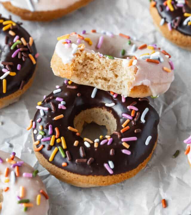 45 degree angle shot of a chocolate glazed and sprinkled donut with a vanilla glazed vegan doughnut with a bite taken out to show the tender crumbed interior.