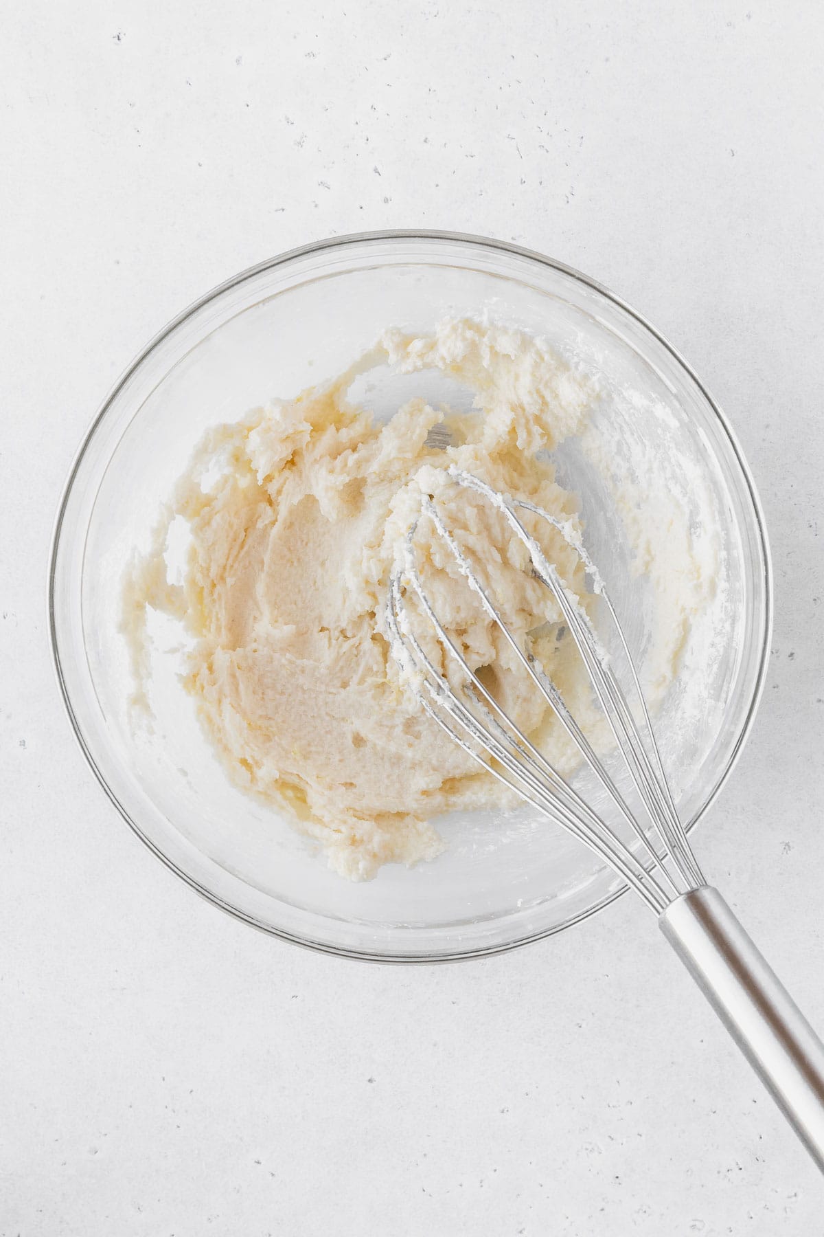 Mixing together the sugar, salt, lemon zest, and eggs in a glass bowl with a silver whisk.