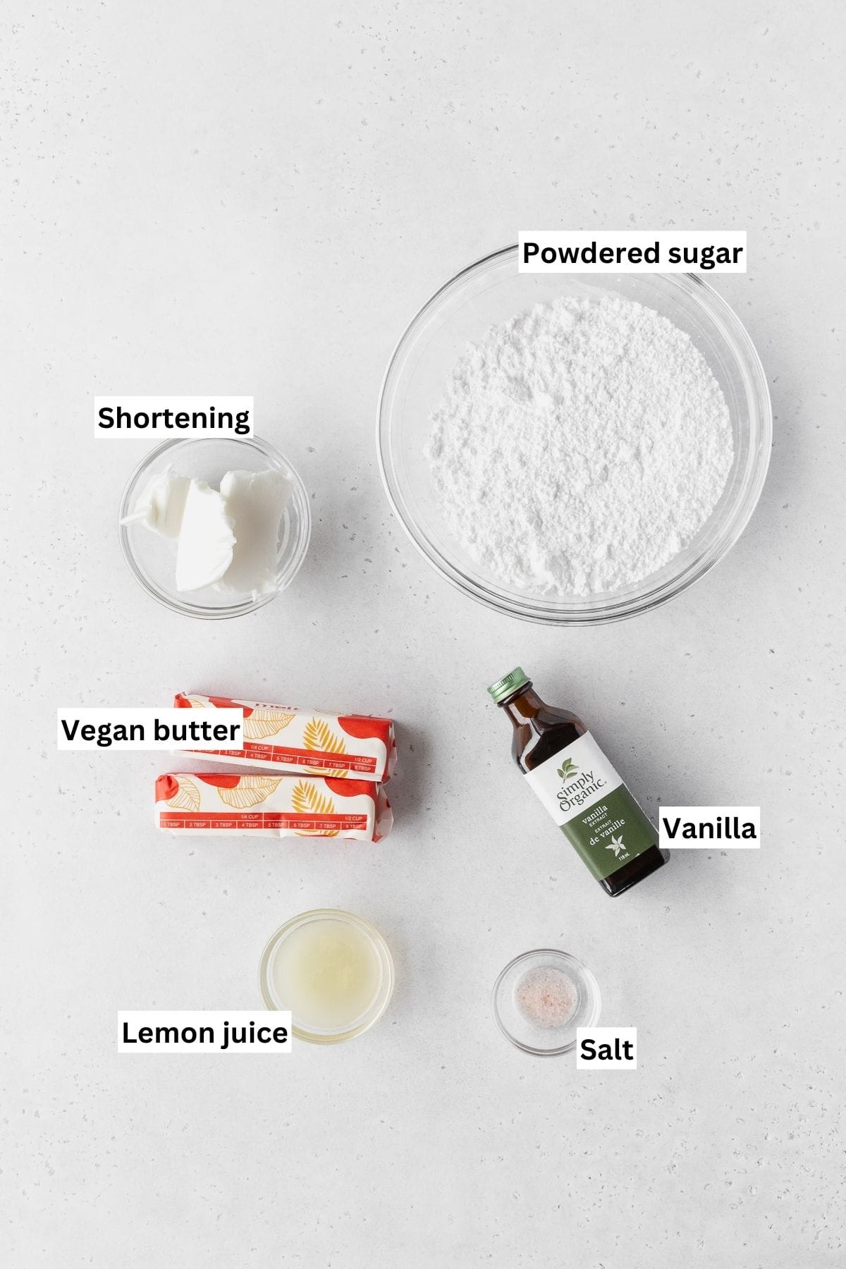 Ingredients for making lemon buttercream frosting on a white table with text overlay.