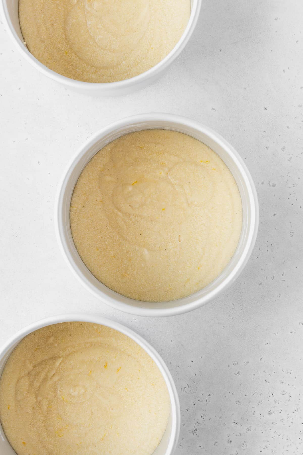 Three 6-inch cake tins filled with lemon cake batter before baking.