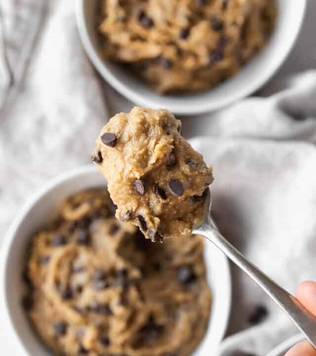 closeup on a spoonful of edible vegan cookie dough with the three bowls filled with it blurred out in the background.