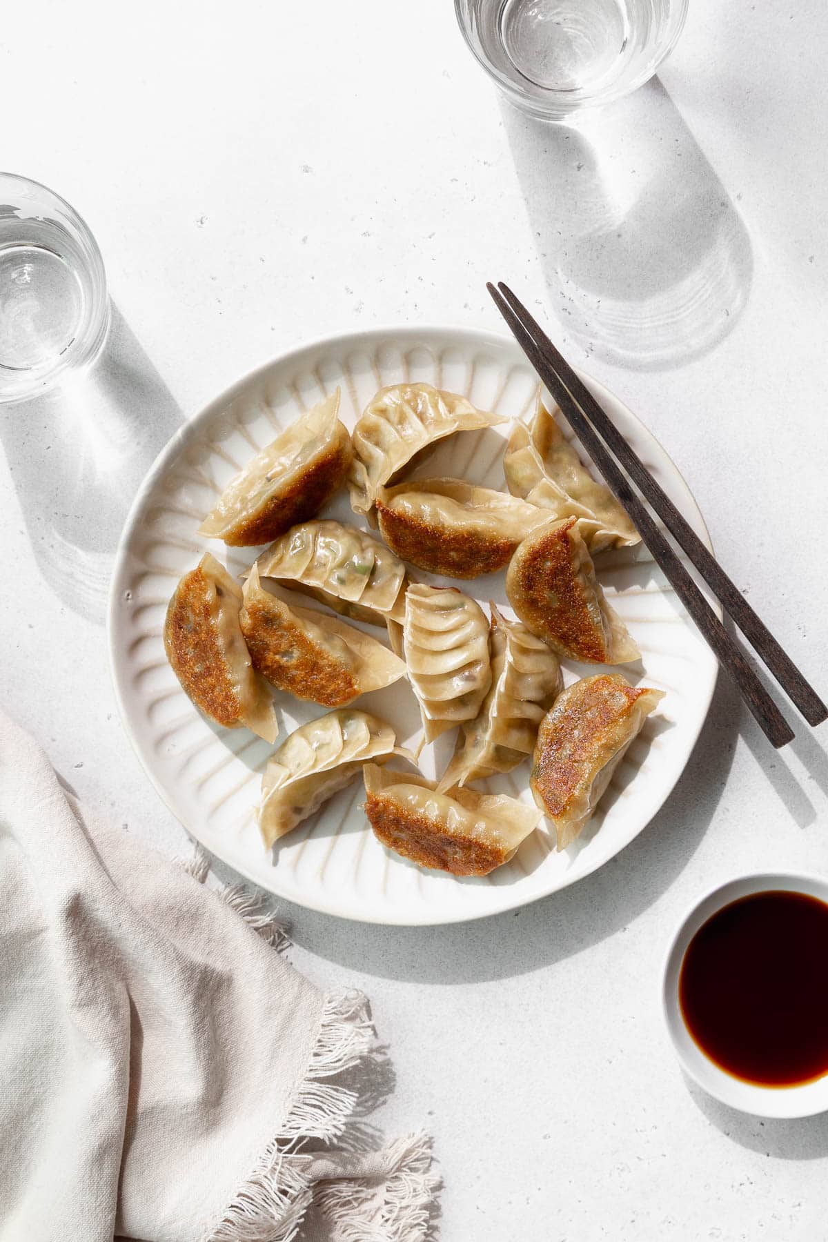 Overhead shot of vegetable gyoza on a white plate with wooden chopsticks.