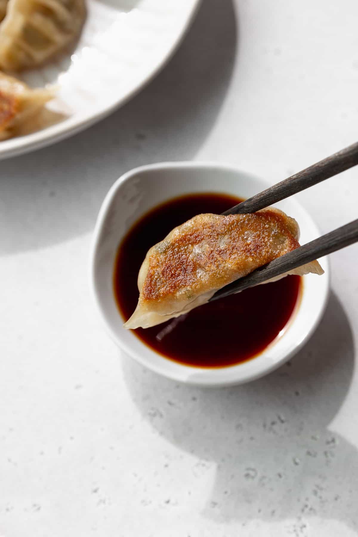 A veggie dumpling being dipped into sauce.