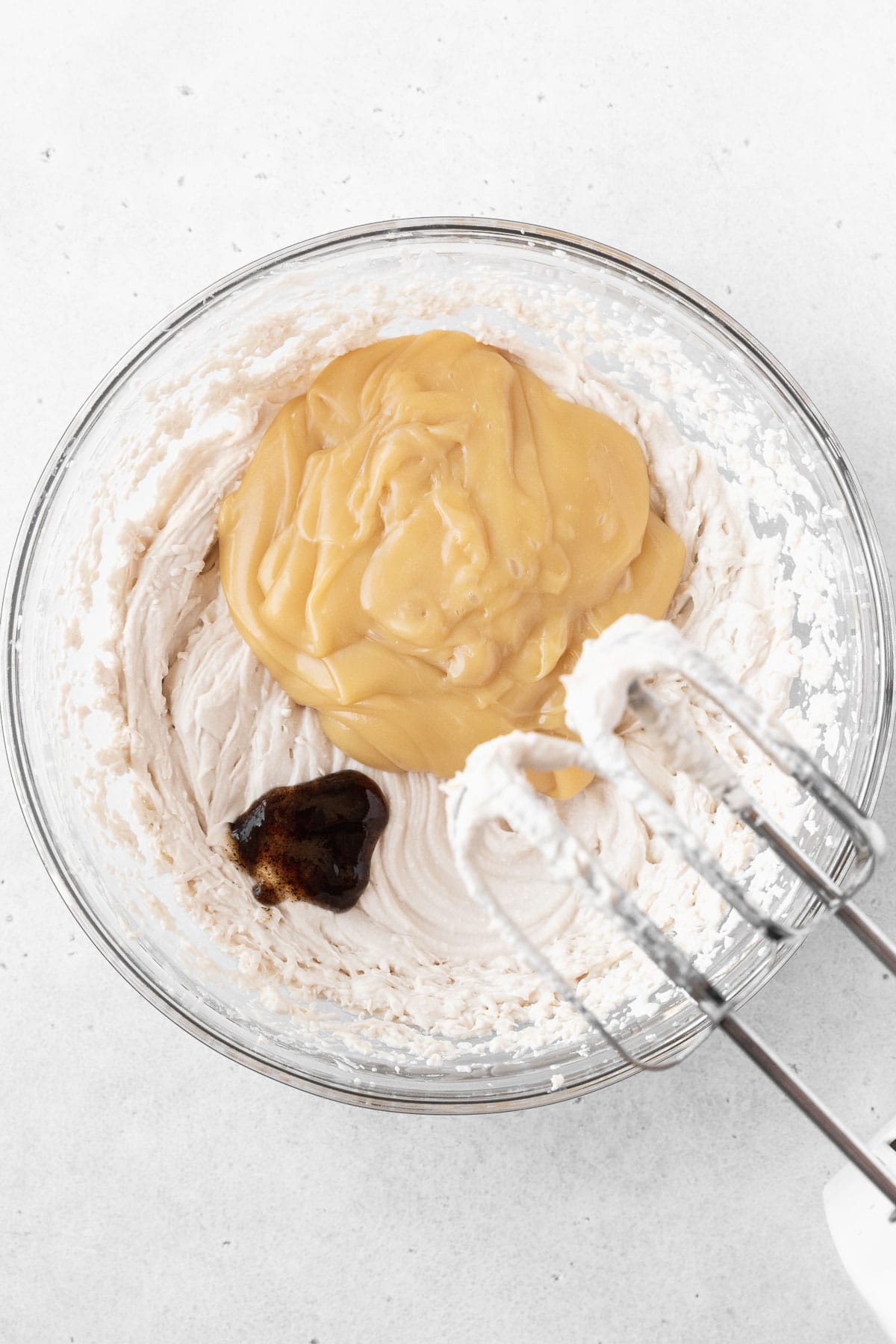 Adding the sweetened condensed oat milk and vanilla to the glass mixing bowl.