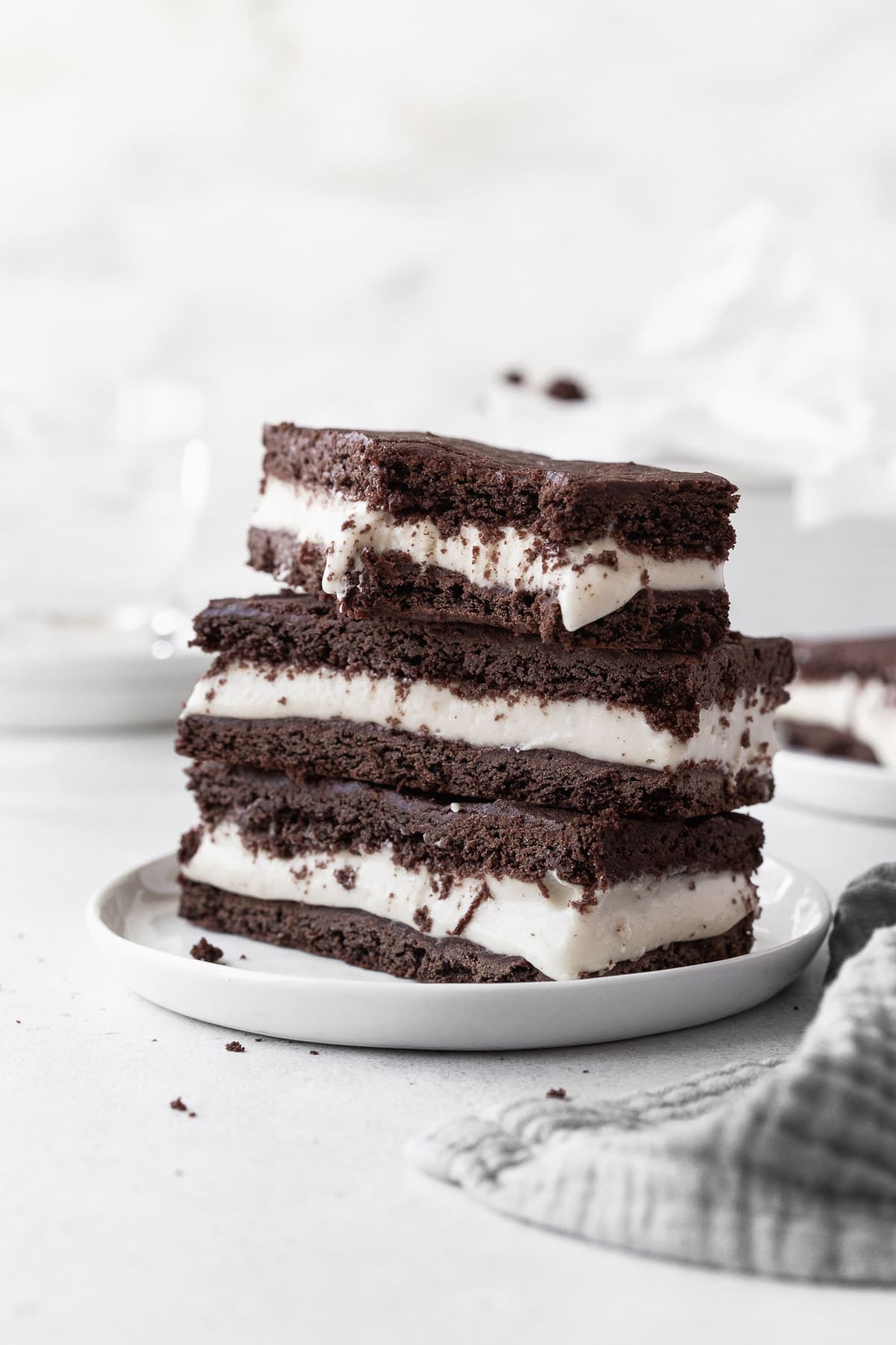 A stack of ice cream sandwich cookies on a small white dish with a large bite taken out of one of the cookies.