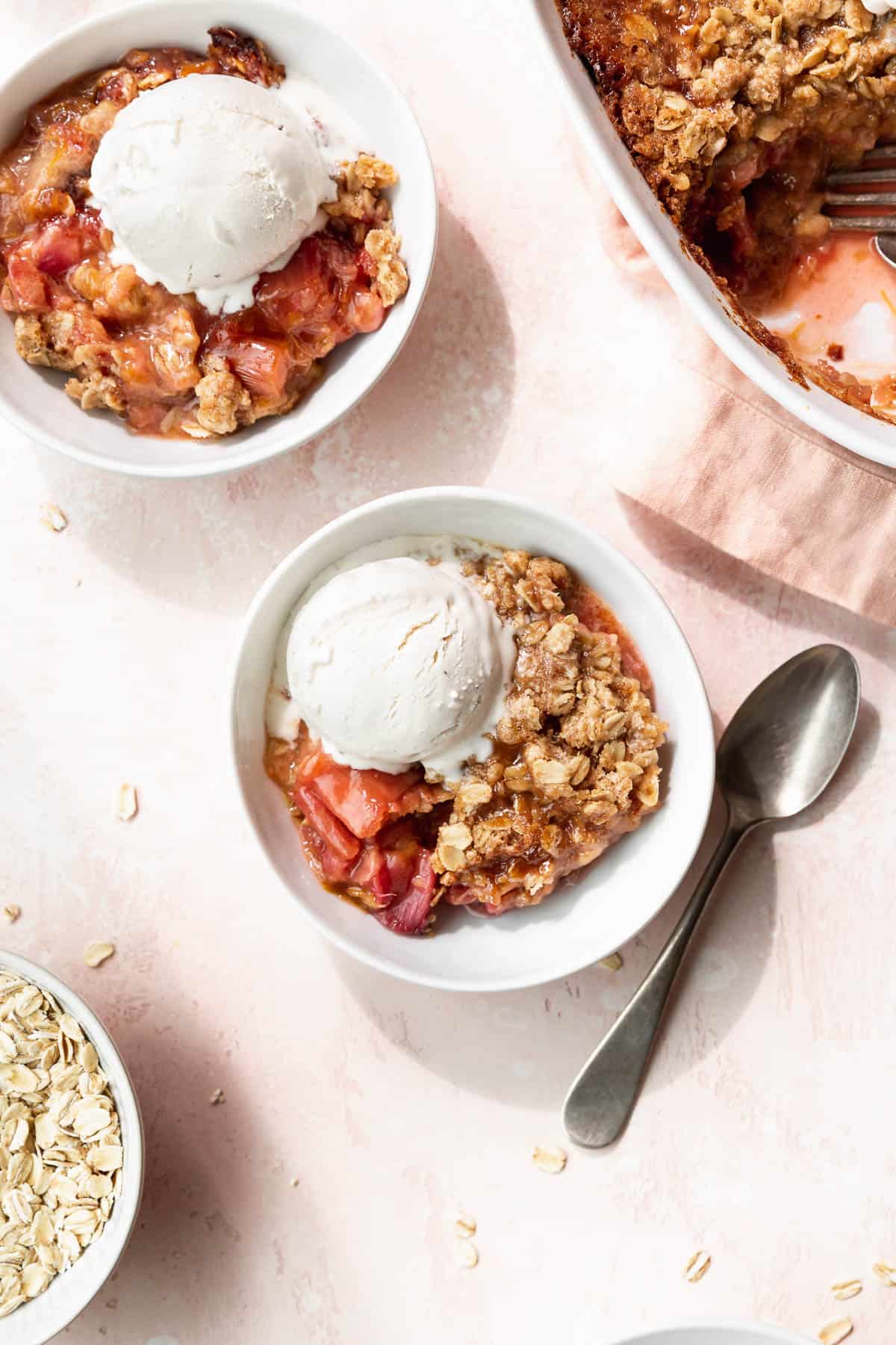 Overhead shot of two bowls of vegan rhubarb crisp topped with vanilla ice cream.