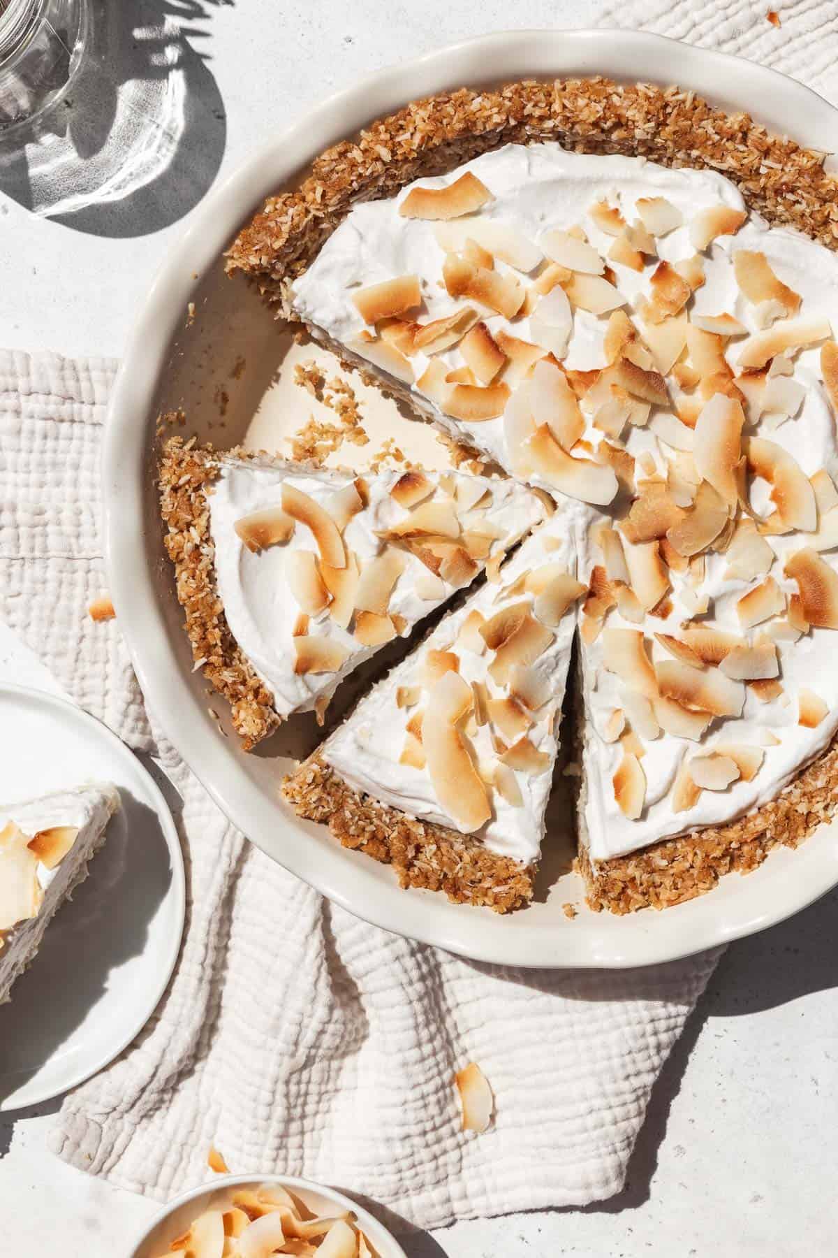 Overhead shot of vegan gluten-free coconut cream pie in a pie dish with two slices prepped to serve.