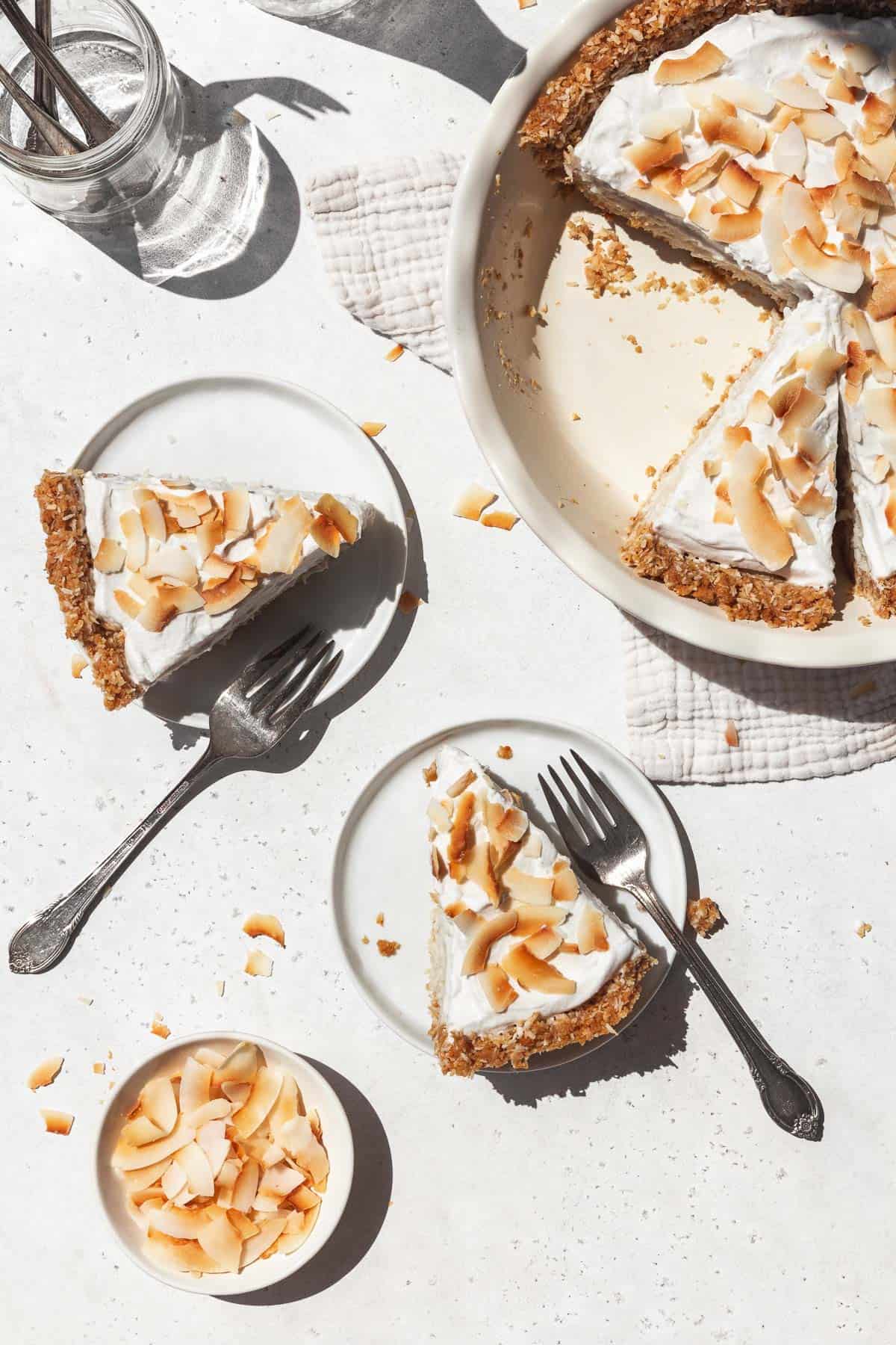 Overhead shot of two dessert plates each with a slice of creamy vegan coconut cream pie topped with toasted coconut flakes.