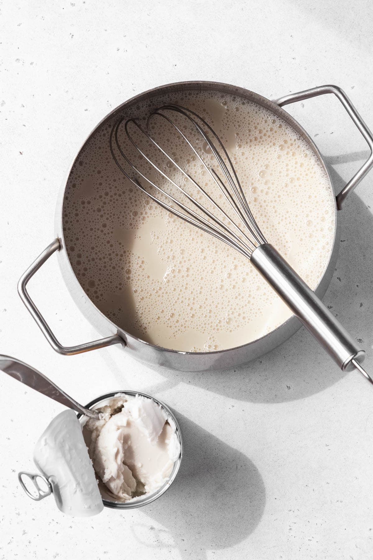 Wet ingredients added to the saucepan for making vegan coconut pudding next to an open can of coconut cream.
